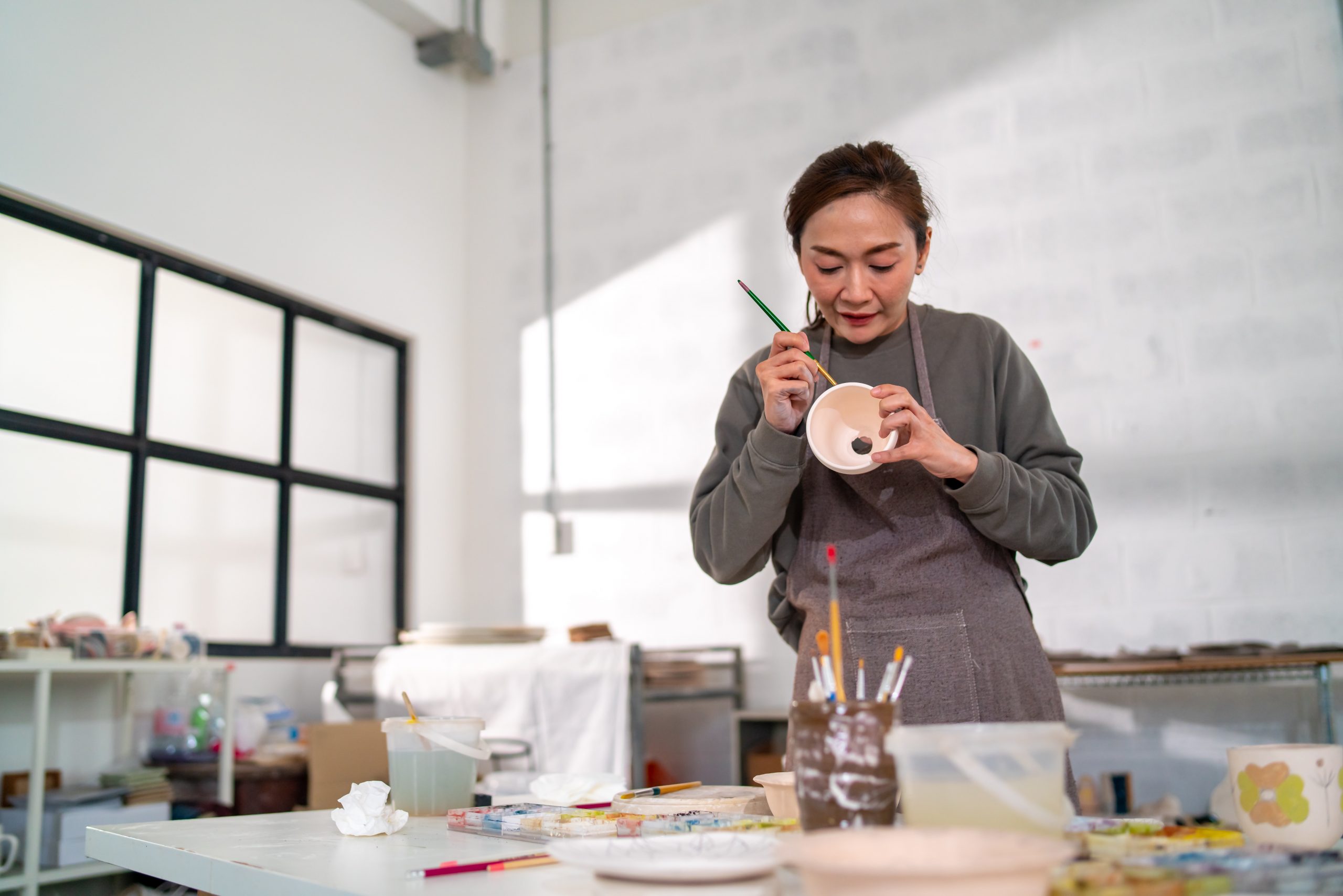 A woman focused on painting a ceramic piece during a pottery workshop, with brushes and art supplies spread out on the table.
