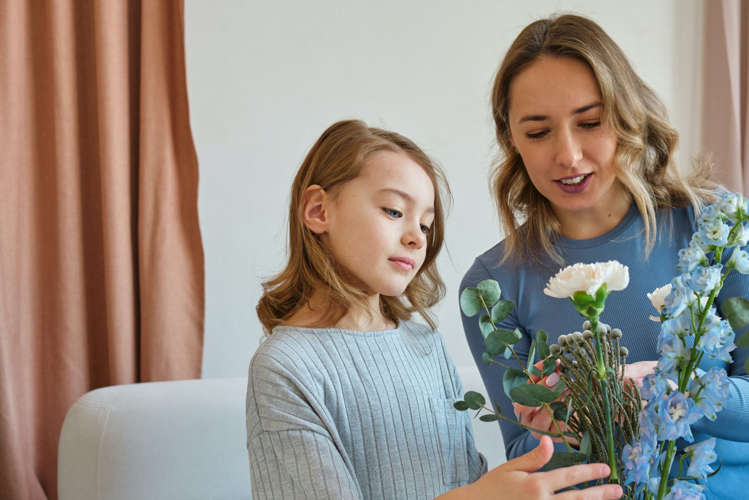 A mother and young daughter smiling as they arrange a bouquet of flowers together, featuring white and blue blooms.