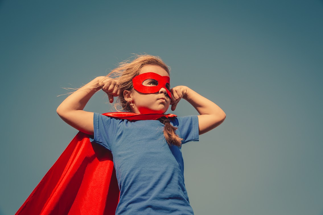 Child in red cape and mask striking a superhero pose, symbolising the power of small actions for charities