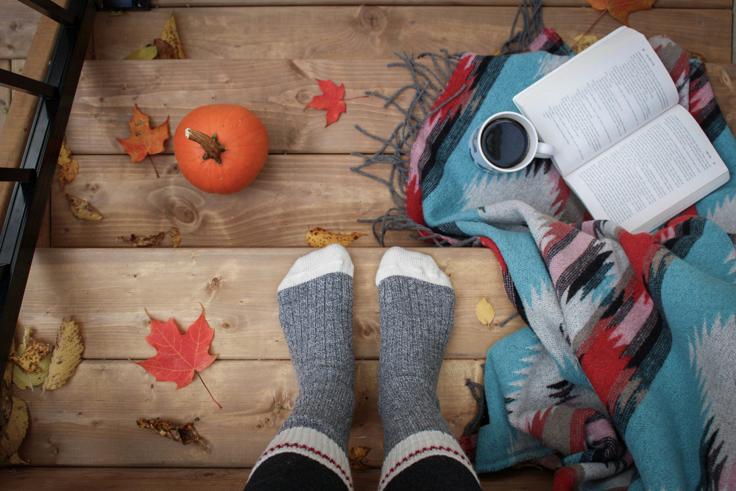 Fall equinox Fundraising Ideas cozy fall scene with socked feet, pumpkins, and an open book