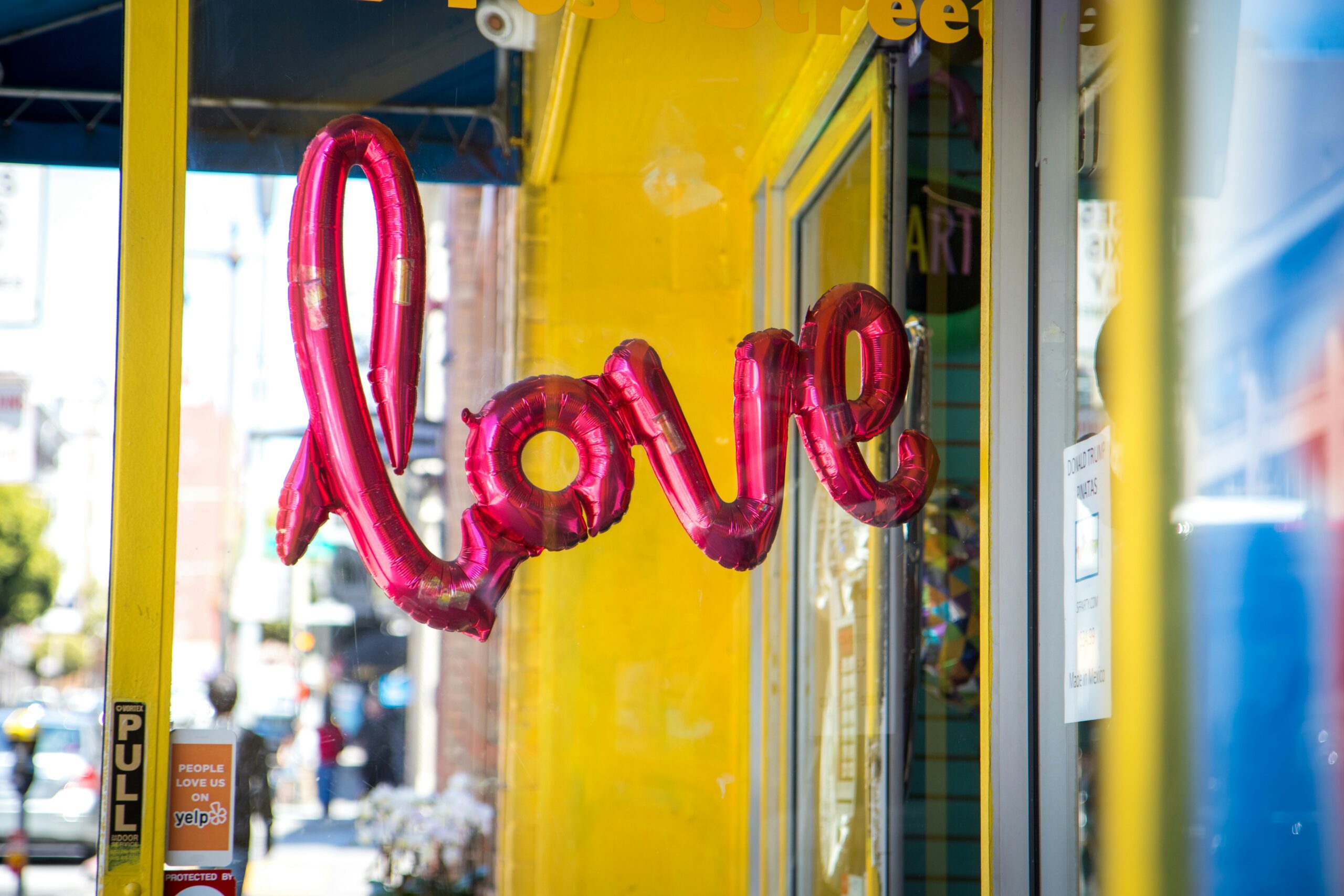 A bright pink helium 'love' ballon hangs in front of a bright yellow shop front