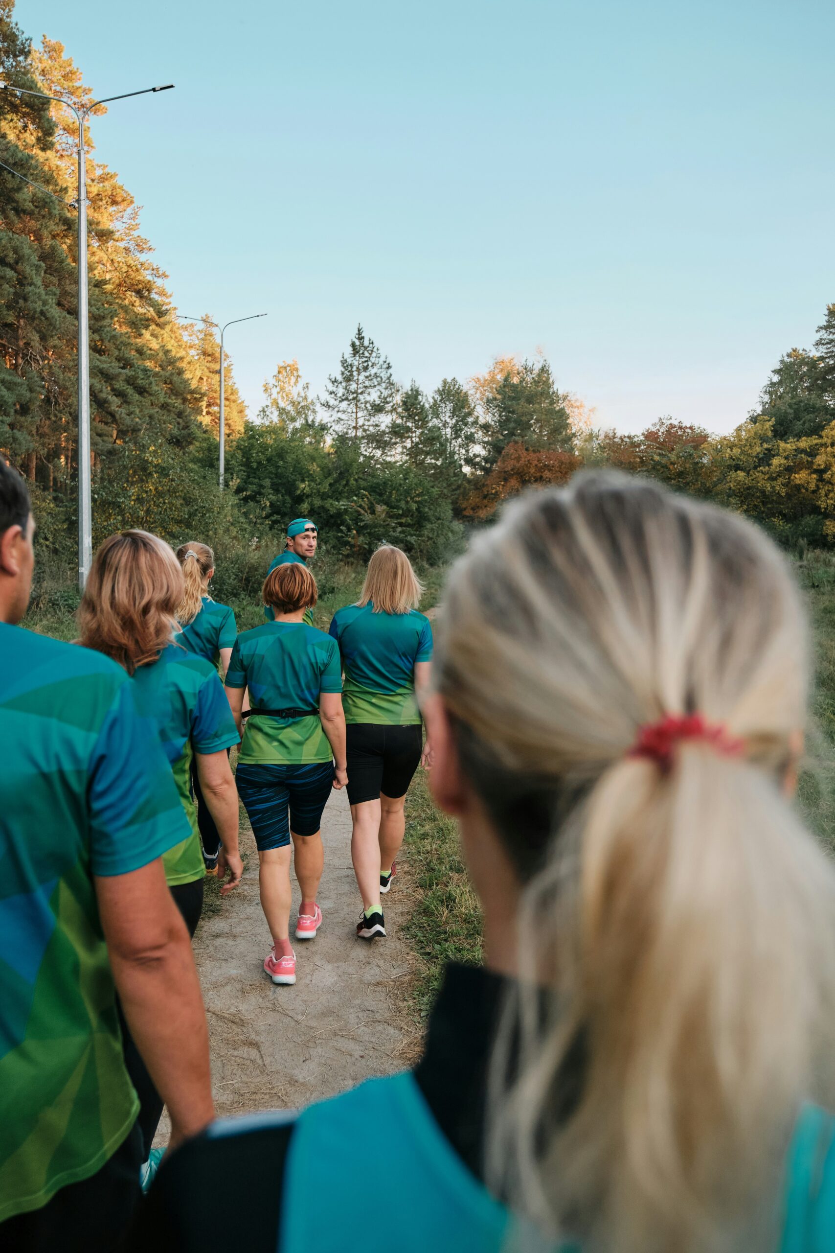 Group of walk-a-thon participants wearing coordinated teal and green t-shirts walking together on a tree-lined path