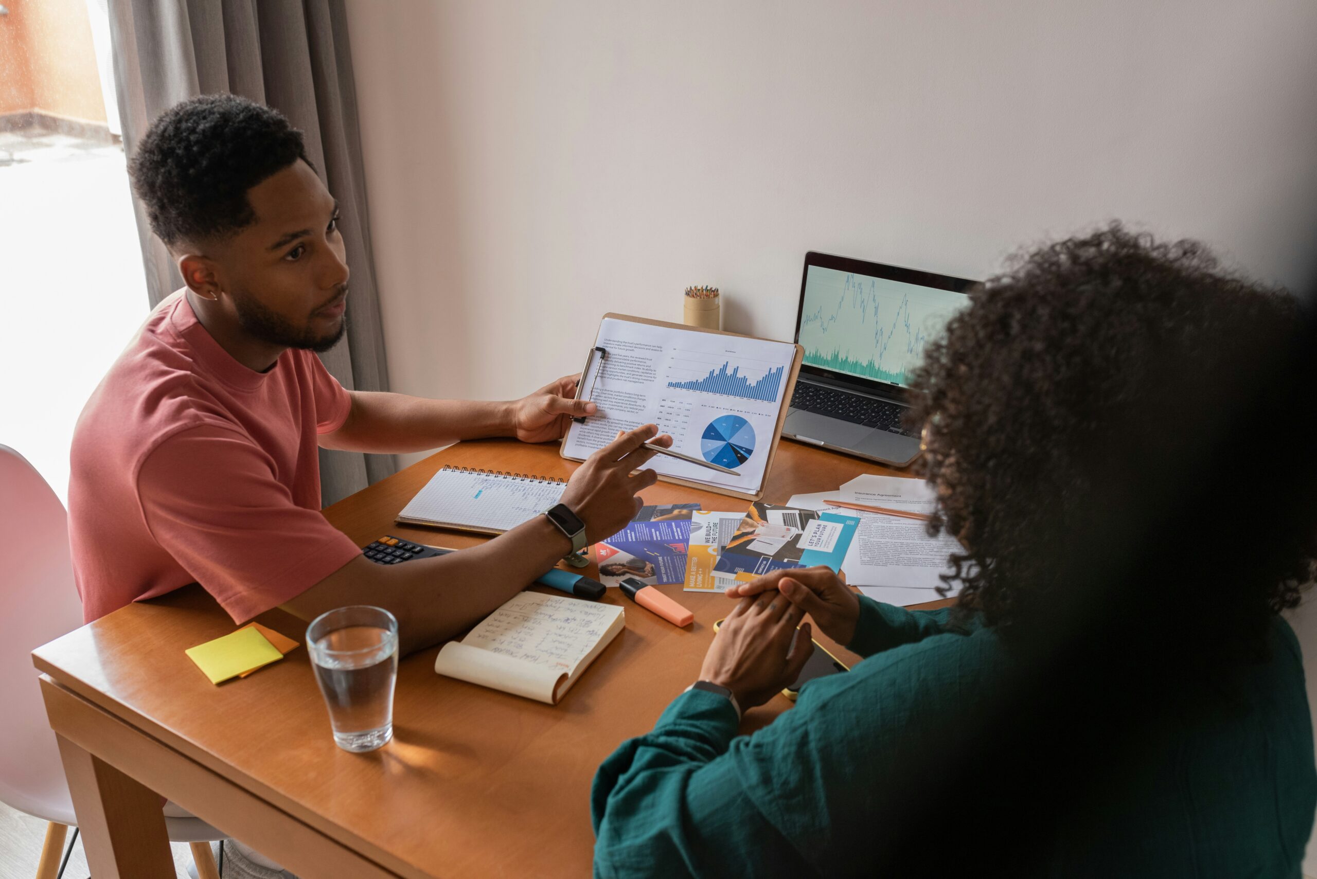 Two nonprofit staff members reviewing fundraising performance data and charts at a desk with laptop, calculator, and printed reports