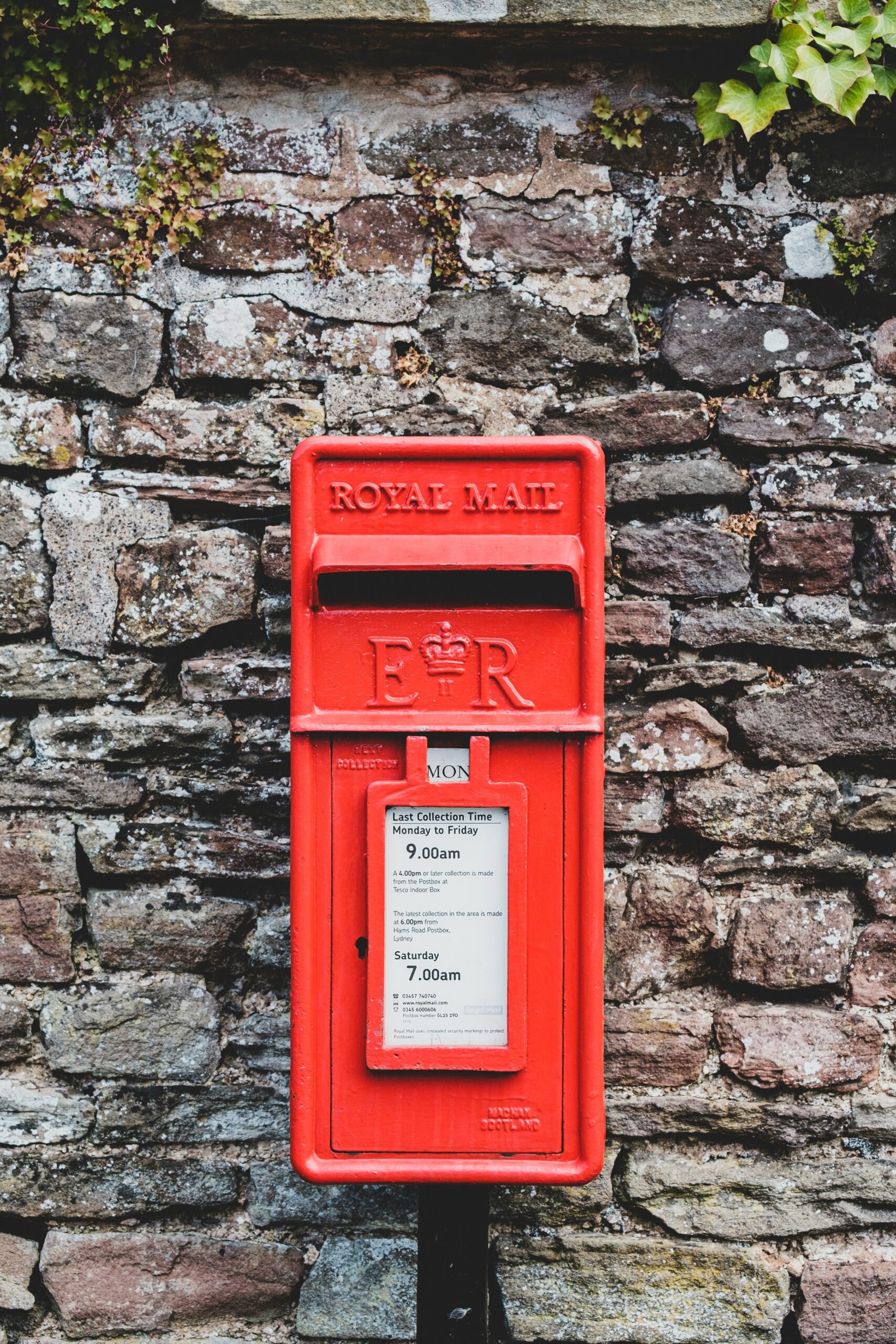royal-mail-postbox-uk-charity-outreach Bright red Royal Mail postbox set against a stone wall in the UK