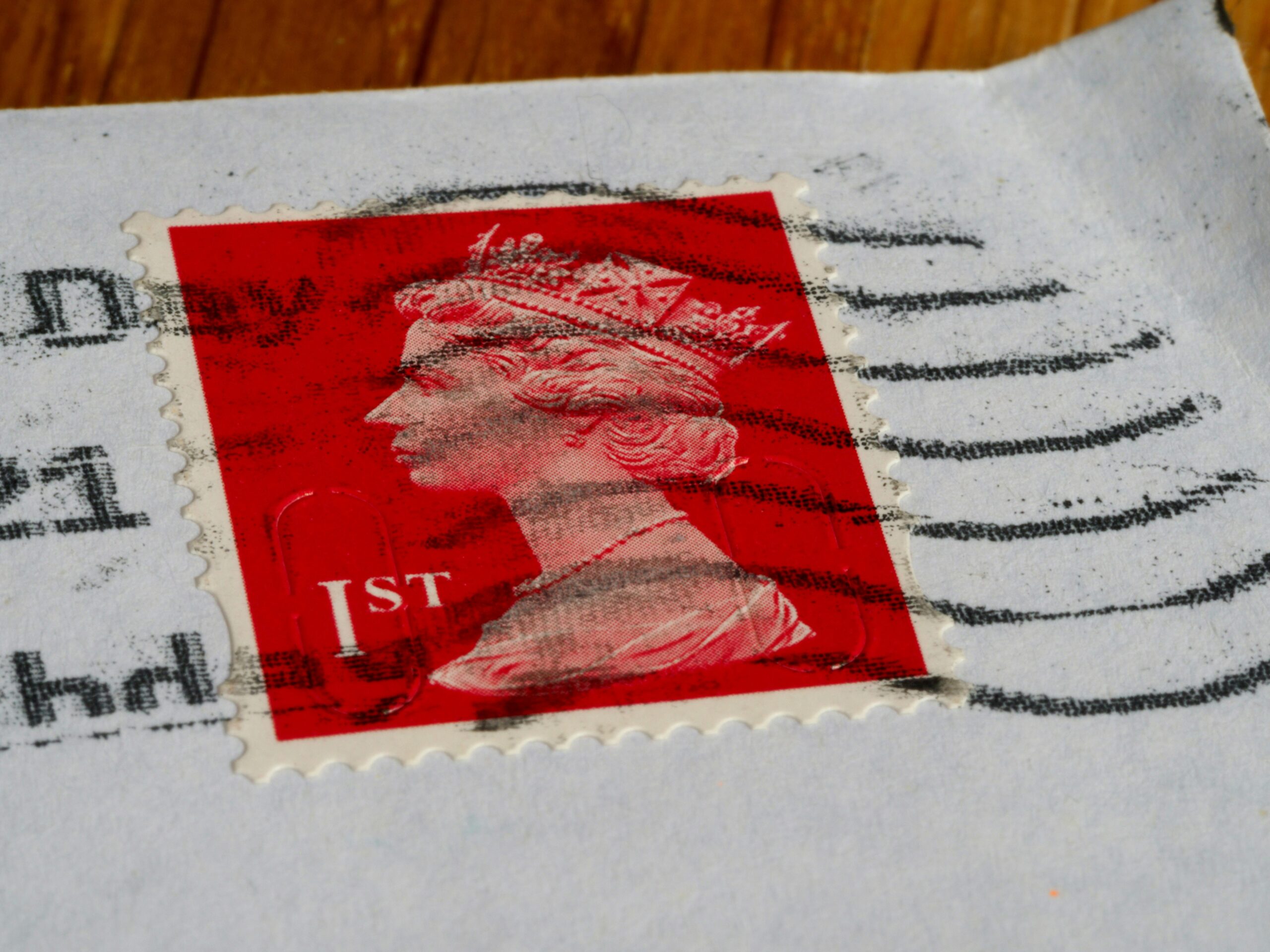 Close-up of a red UK first class stamp with Queen Elizabeth II’s profile, postmarked on a white envelope